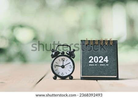close up 2024 small black calendar and alarm clock on table, happy new year and holiday season, planning and manage time to success business concept