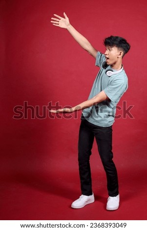 Excited Asian man showing blank space aside for advertisement standing over crimson background Royalty-Free Stock Photo #2368393049