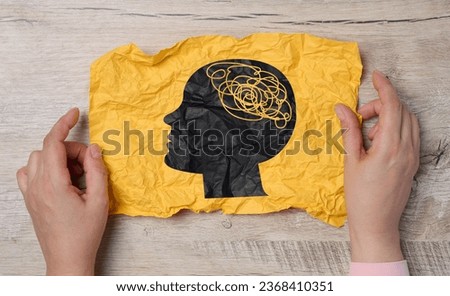 A female hand holds a crumpled paper with a black silhouette of a person's head and tangled threads inside, representing the concept of human mental health Royalty-Free Stock Photo #2368410351