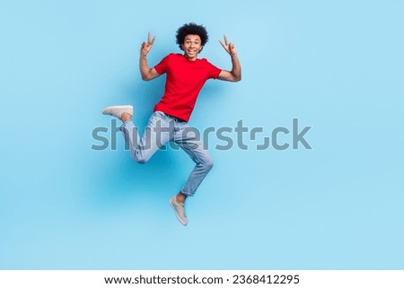 Full length photo of optimistic cheerful nice person wear red t-shirt jeans jumping showing v-sign isolated on blue color background