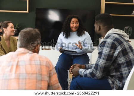 Diverse group of friends and female therapist with tablet in group therapy session. Mental health, therapy, friendship and support,communication, unaltered. Royalty-Free Stock Photo #2368422291
