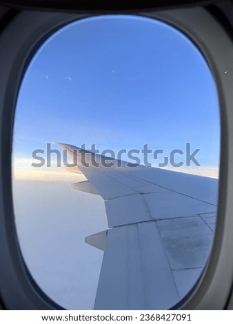 View from an airplane’s window during a soft sun rise with a thick carpet of clouds. An airplane wing occupies half of the picture.