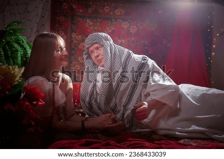 Portrait of young arabian muslim couple in traditional clothes in cozy red room. Fhoto shoot in easten style with male and female model like in a harem with a sultan and an odalisque. Partial focus