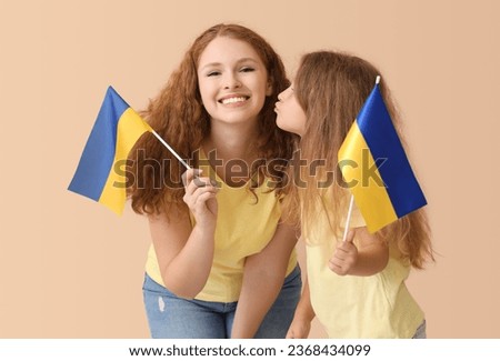 Happy little girl kissing her mother with Ukrainian flags on beige background