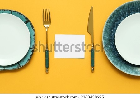 Composition with blank card, plates and cutlery on orange background