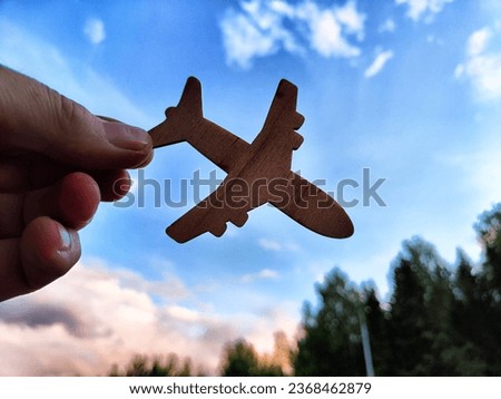 Hand holding toy wooden airplane plane and blue sky with forest background. The concept of flying on airplane, travel, leisure, adventure. Blurred picture, partial focus
