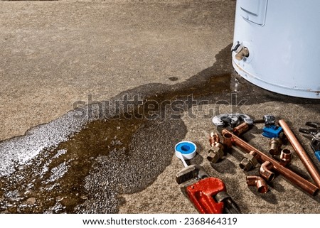 Water leaking from the plastic faucet on a residential electric water heater with tools to repair the appliance.  Royalty-Free Stock Photo #2368464319