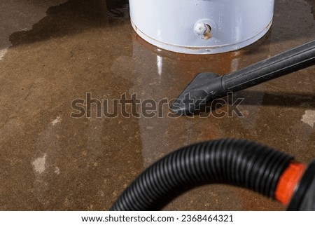 A wet-dry vacuum being used to clean up water from a leaking residential electric water heater. Royalty-Free Stock Photo #2368464321