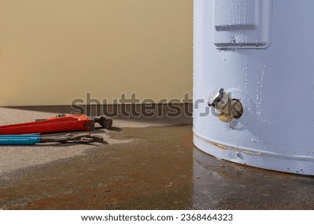 Water leaking from a residential electric water heater with a couple plumbers tools. Royalty-Free Stock Photo #2368464323