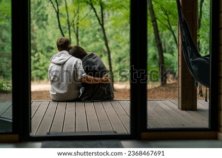 Man and woman in love sitting with their backs to the camera on a terrace overlooking the forest with plaids cuddling and talking