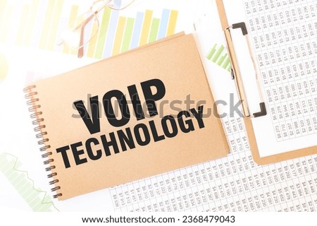 Business up graph on a sheet of craft colour Notepad with VOIP TECHNOLOGY sign. Notepad on desk with financial documentation