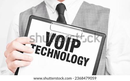 VOIP TECHNOLOGY inscription on a notebook in the hands of a businessman on a gray background, a man points with a finger to the text