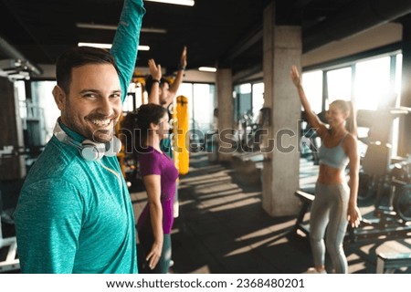 Group of smiling athletic people following warming up instructions of their beautiful female fitness coach before gym workout. Man looking at camera smiling during exercise fitness class. Royalty-Free Stock Photo #2368480201