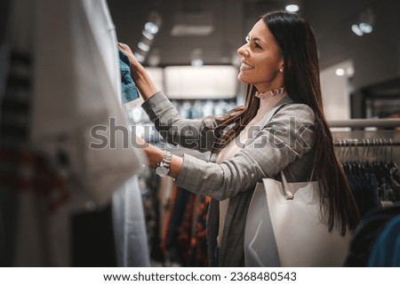Beautiful happy young woman with long dark hair looking at the clothes while shopping on a weekend sales in a shopping mall.