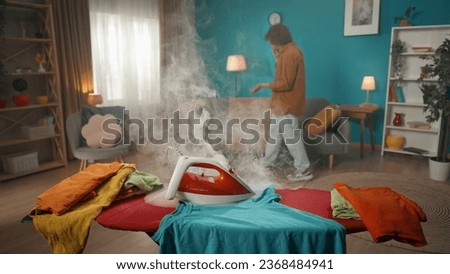 Young guy in the background talking passionately on the phone. In the foreground is an iron on an ironing board that is beginning to smoke. The man doesn't notice what is happening