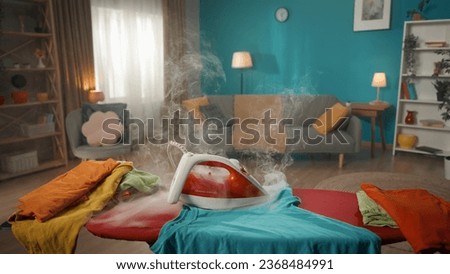 The photo shows a close-up of an iron standing on an ironing board. It is smoking, but there is no one in the room and no one notices it. Someone forgot to turn off the iron. Electrical appliance Royalty-Free Stock Photo #2368484991
