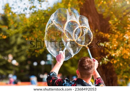 An animator launches large soap bubbles at a children's party using two rings. Autumn nature on a sunny day. The shape of rainbow balls is similar to a heart. The concept of an animator's work.