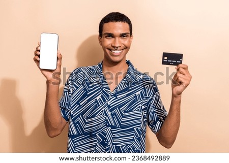 Photo portrait of handsome young guy hold telephone credit card eshop wear trendy blue print outfit isolated on beige color background