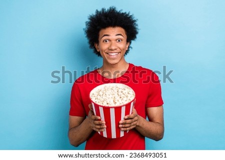 Photo of impressed funky guy with afro hairstyle dressed stylish red t-shirt hold popcorn watch movie isolated on blue color background