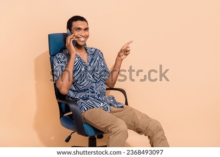 Photo of excited pretty man wear print shirt speaking modern gadget pointing empty space isolated beige color background