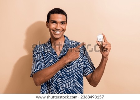 Photo portrait of handsome young guy finger point white little house wear trendy blue print outfit isolated on beige color background
