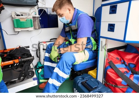 Tired paramedic in a protective mask sits in an ambulance
