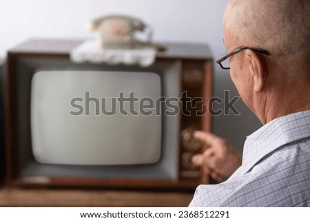 elderly man turns on and watches old retro analog TV with blank screen for designer, white background, 1960-1970, stylish mockup, template for video, Retro Technology in Everyday Life Royalty-Free Stock Photo #2368512291