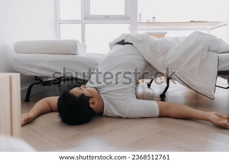 Asian man sleeping lying on floor, having deep sleep dream, fall down from white bed at apartment. Royalty-Free Stock Photo #2368512761