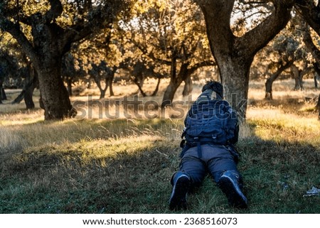 An unrecognizable young boy lying on the ground taking pictures of the deer. Riofrio Forest, Segovia