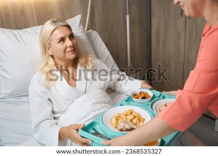 Nurse serves tray of food to woman on hospital bed