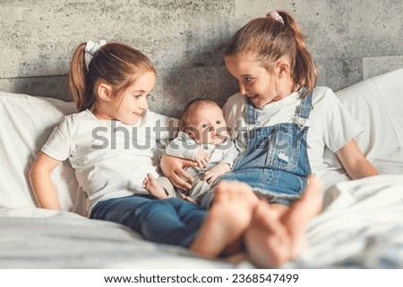 The two sisters sit on bedroom with newborn son at home