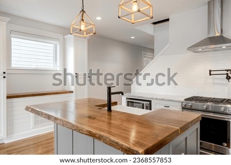Luxury Modern White Kitchen with Organic Raw Edge Wood Countertop and Black Sleek Faucet. Subway Tile Backsplash and Pot Filler Royalty-Free Stock Photo #2368557853
