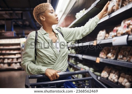 Grocery, shopping cart and woman in supermarket at shelf for food at retail convenience store. Groceries, serious and African customer on trolley at shop to check product price, sales choice and cost
