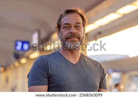 Street portrait of an elderly bearded man 50-55 years old on a blurred background of a train station.