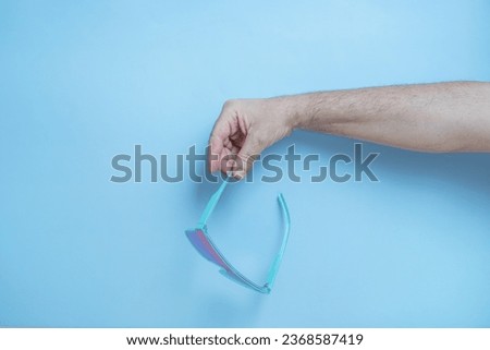 A man's hand holding blue sunglasses