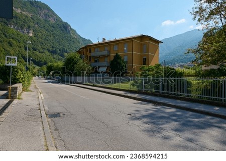 Horizontal panoramic photography. A road in Italian town in Lombardy with view of a residence or mansion against Italian Alps background. Mountains. Sky. Nature background. Travel and tourism concept