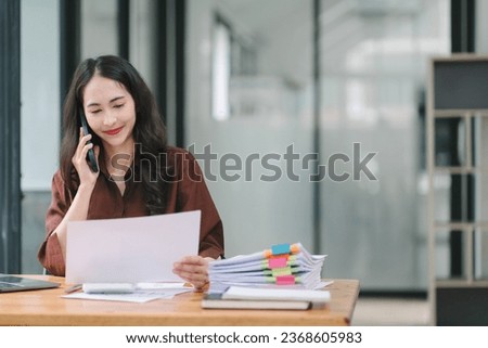 Young adult Asian businesswoman, secretary, sales manager, business consultant, engaging in a phone conversation with a client at the office