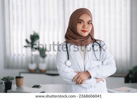 Portrait of a confident Asian Muslim female doctor with her arms crossed, wearing a brown hijab