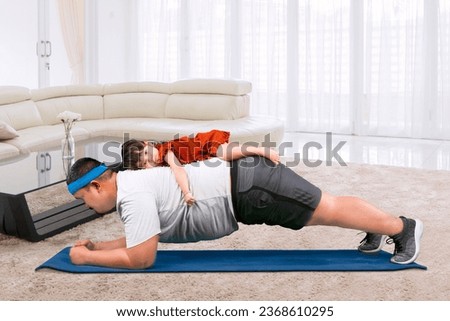 Cute moment Overweight father doing plank exercise while daughter on his back at home Royalty-Free Stock Photo #2368610295