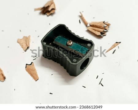 Black sharpener and pencil shavings on white paper, a minimalist and creative concept for stationery and art enthusiasts.