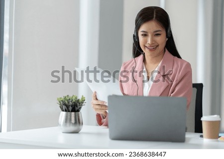 Asian businesswoman employee or executive using laptop computer and wearing headset video call explaining online meeting or online training. Document work in the office