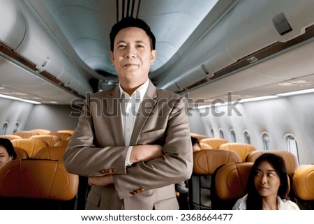 Portrait of Asian senior businessman standing with arms crossed on aisle inside airplane, male passenger in suit on business trip in aircraft, businesspeople traveling with airline transportation. Royalty-Free Stock Photo #2368664477