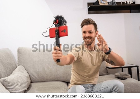 Streamer waving to the camera while recording online with a mobile sitting on the sofa at home