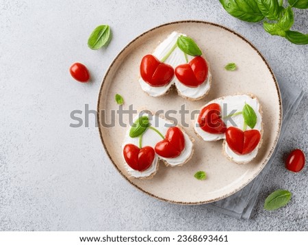 Heart shaped sandwiches with cherry hearts made of tomatoes, basil leaves and cream cheese spread. Saint Valentine's day breakfast. Festive vegetarian food. Love day decoration. Top view, copy space.