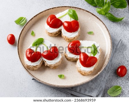 Heart shaped sandwiches with cherry hearts made of tomatoes, basil leaves and cream cheese spread. Saint Valentine's day breakfast. Festive vegetarian food. Love day food. Close up view.