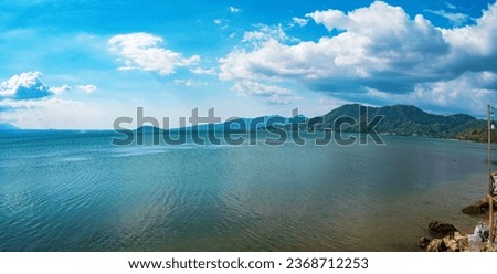 Stunning panorama of the coastline in Bima Bay, located in Palibelo District. On the horizon there is a view of mountains under a bright blue sky, scattered clouds and a blue sea.