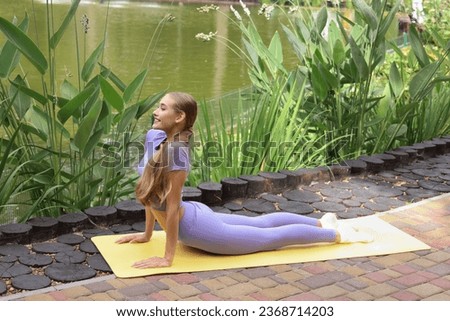 Calm young blonde  woman with closed eyes is practicing  stretch on the back pain yoga, breathing, exercising in the park, enjoying peace and freedom. She is relaxing.