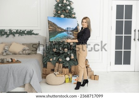 woman holding a photo canvas on the background of a Christmas interior.