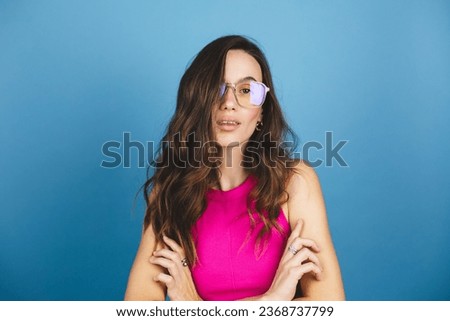 Photo portrait of curly brunette woman entrepreneur serious calm with crossed hands wearing glasses and pink top isolated on bright blue color background. 