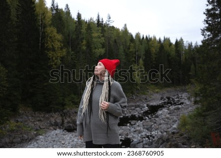 beautiful young Asian woman with African braids in a red hat against the background of a war forest and a river.